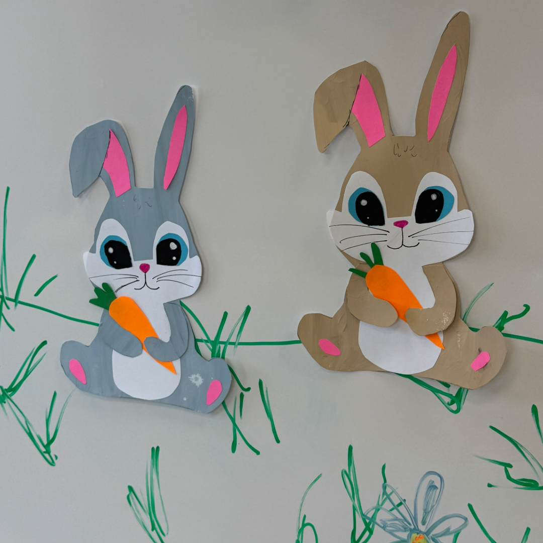 A gray bunny and a light brown bunny both holding carrots on white background with hand=drawn grass around them